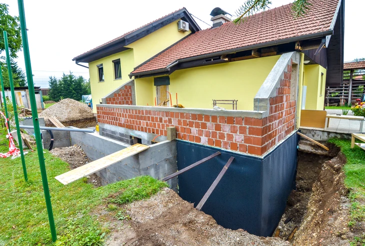 Chantier de construction résidentielle en cours avec extension d'une maison jaune à toit de tuiles